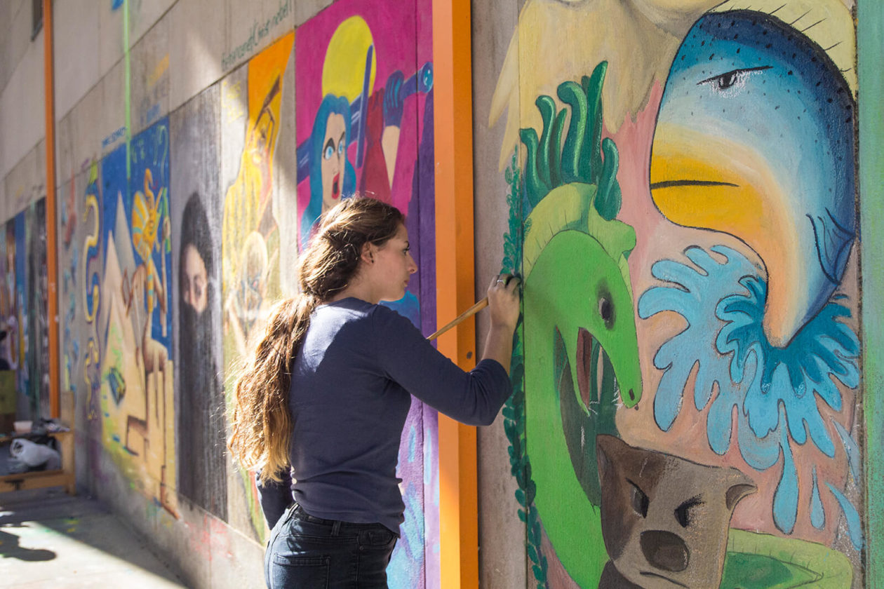 Young woman painting a mural on an outside wall.