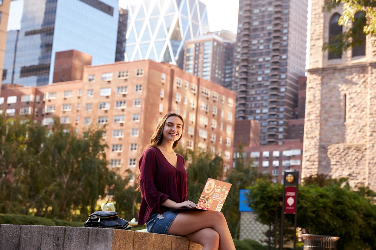 Student with a laptop sitting outside large buildings.