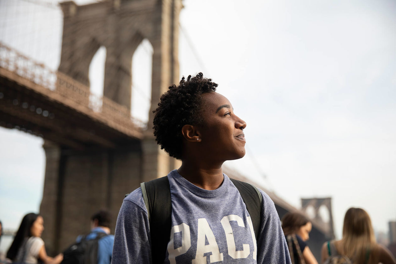 Student standing in front of a bridge wearing a Pace University sweatshirt.