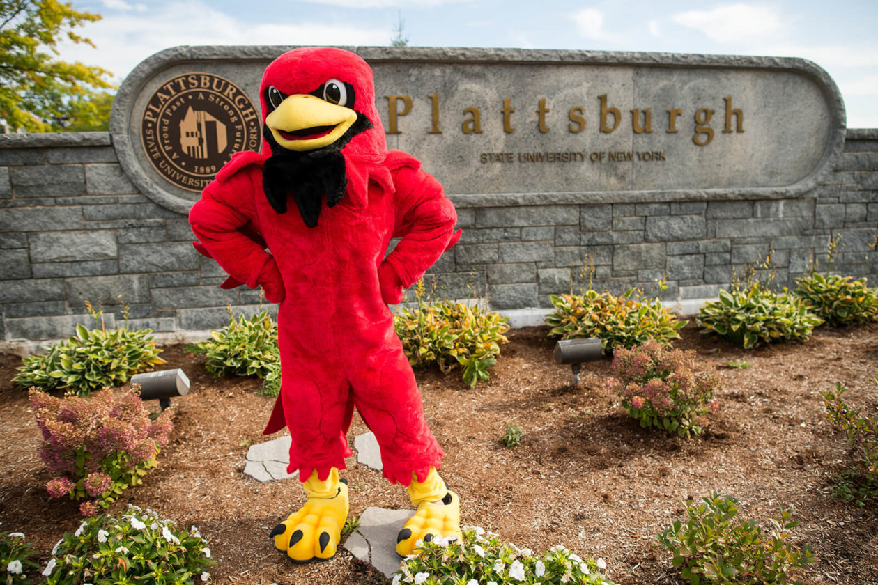 SUNY Plattsburgh mascot standing in front of SUNY Plattsburgh stone sign.